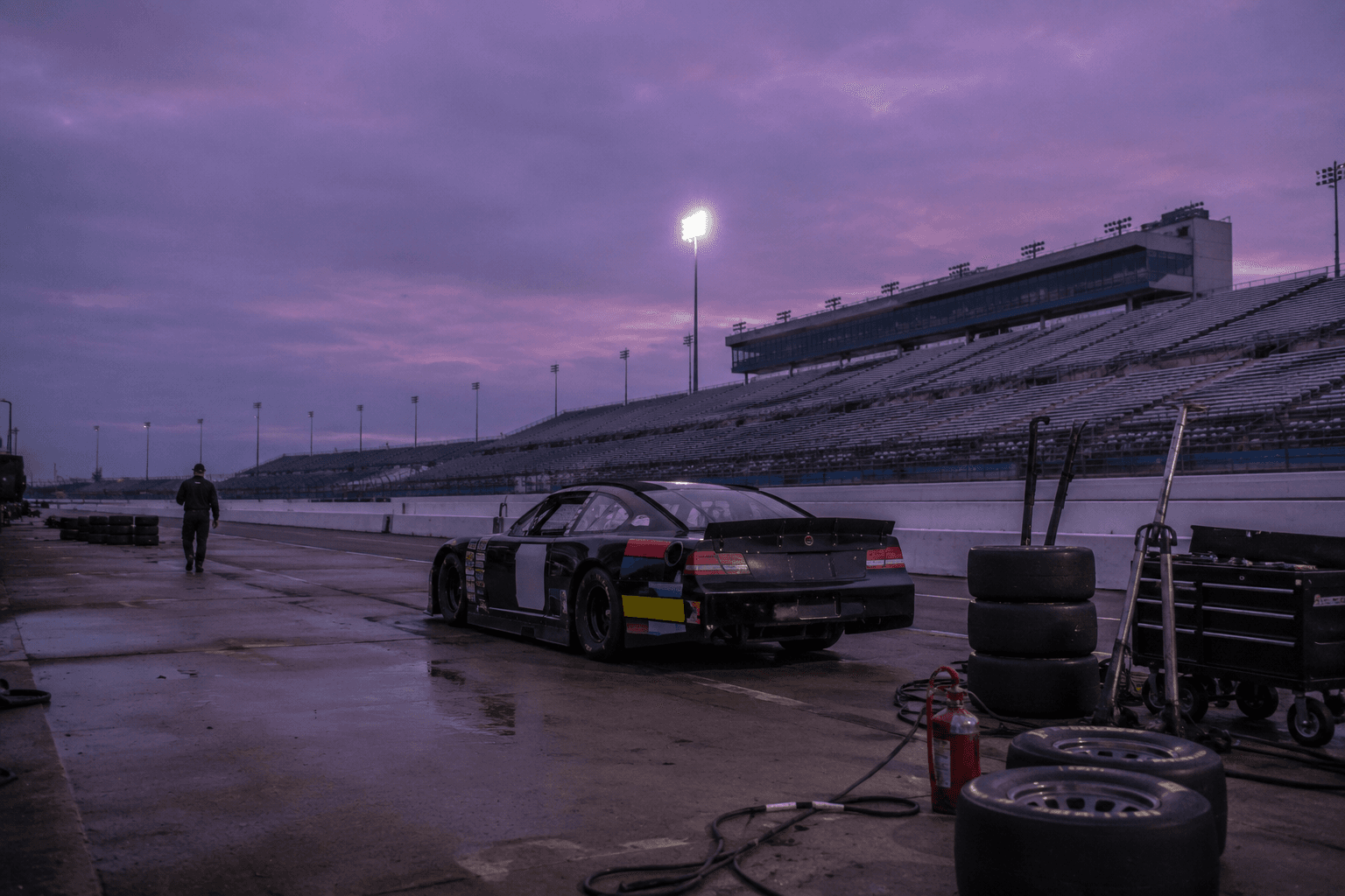 A solitary race car parked alone in an empty pit lane at twilight, covered in generic sponsor decals